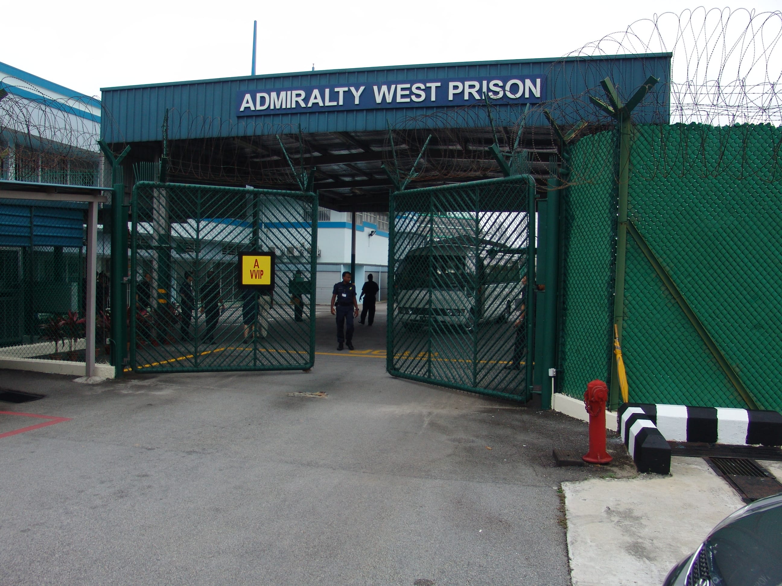 Entrance to Admiralty West Prison with barbed wire fence and a yellow sign saying "A WIP" on the gate.